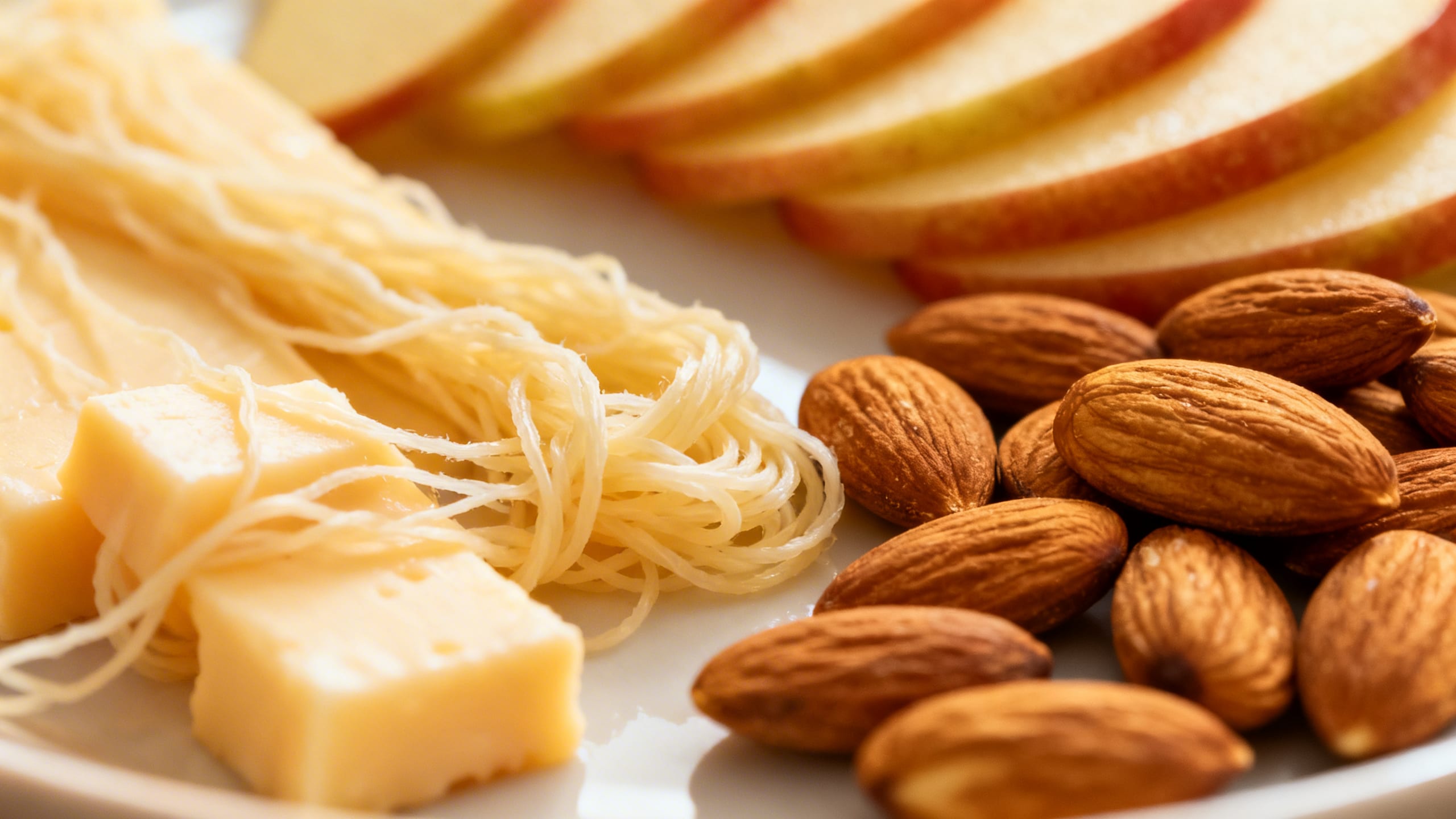 a balanced snack plate with string cheese, apple slices, and almonds