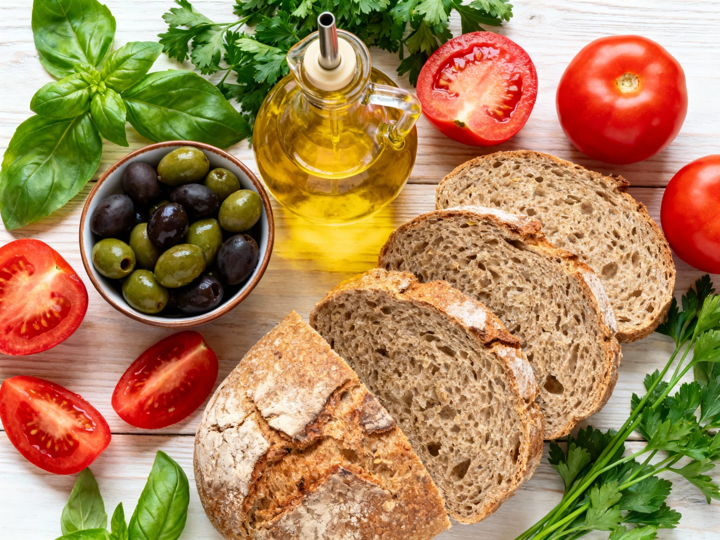 a vibrant flat lay of classic Mediterranean ingredients like olives, fresh tomatoes, herbs, olive oil, and whole wheat bread